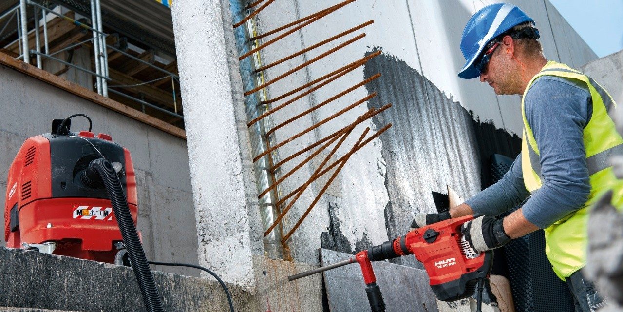 En arbejder i sikkerhedsudstyr borer huller i en betonflade som forberedelse til eftermonteret armering.