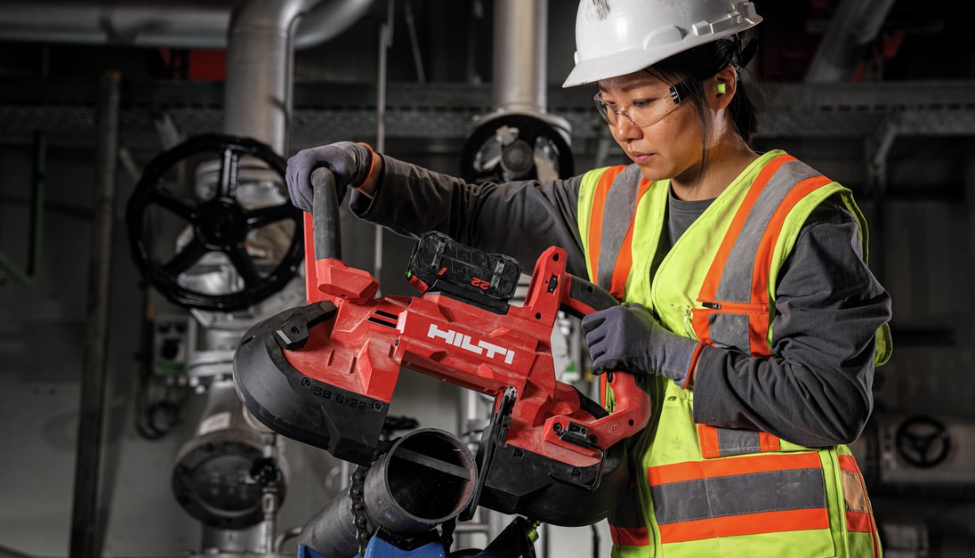 Woman using band saw to cut metal pipe