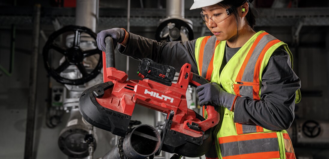 Woman using band saw to cut metal pipe