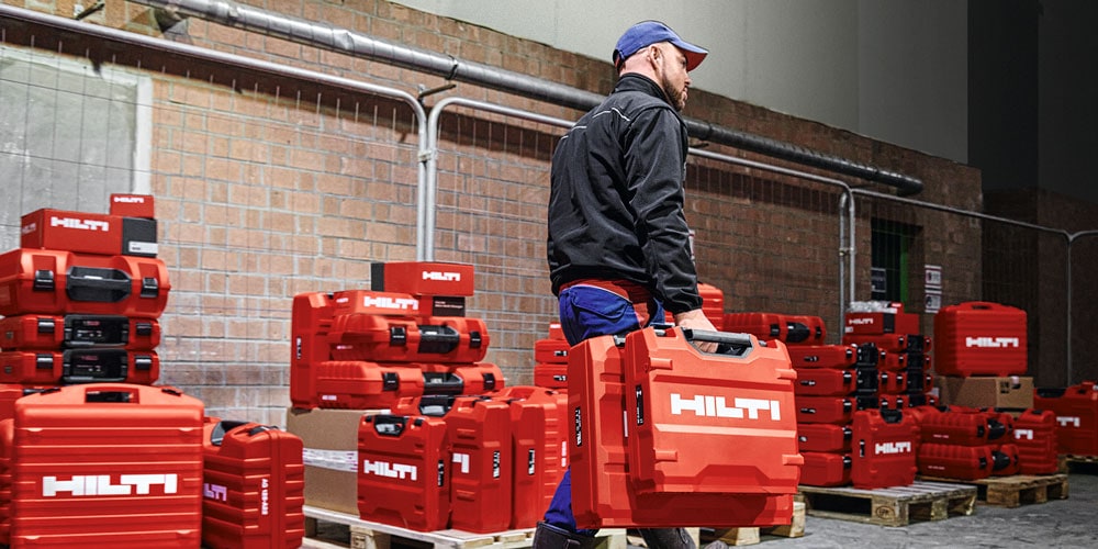 Mand går med en Hilti kuffert med flere hilti kufferter i baggrunden