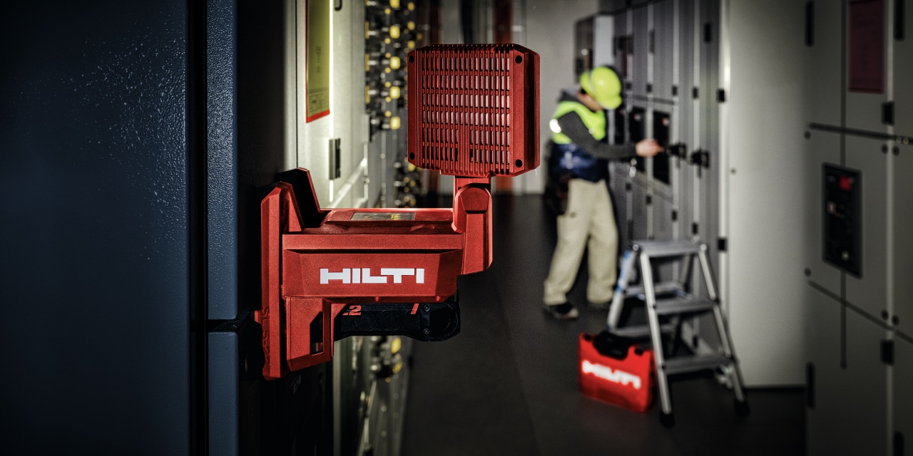 MAND ARBEJDER I ET MØRKT RUM MED EN RØD HILTI ARBEJDSLAMPE PÅ VÆGGEN