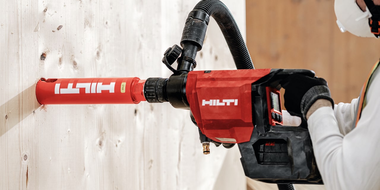 Person bruger et rød hilti diamantboremaskine i en betonvæg